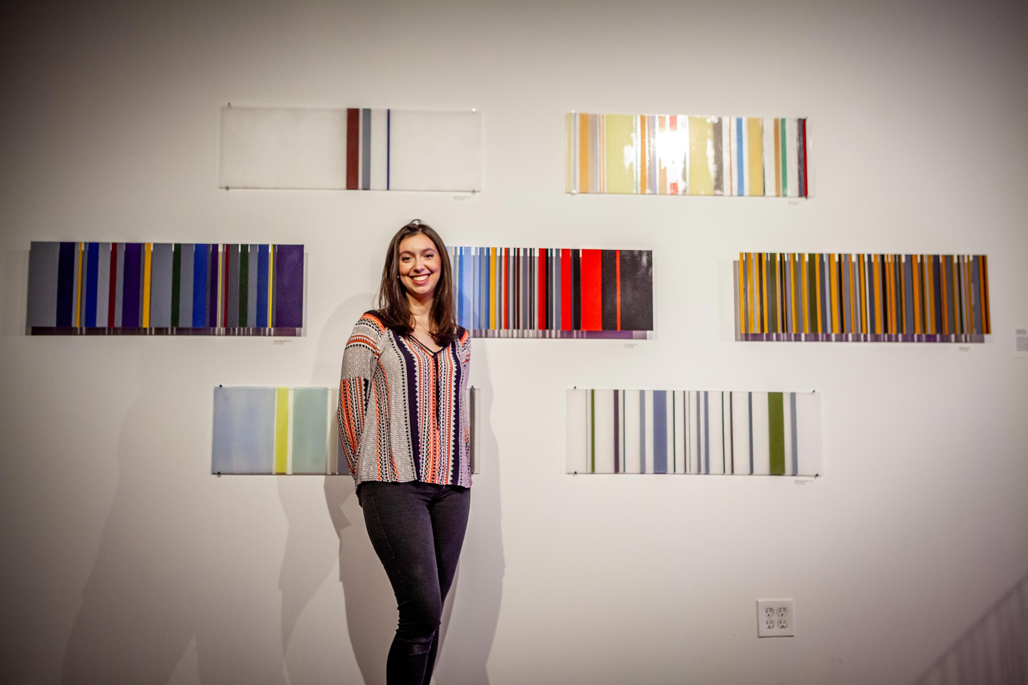 student artist standing in front of her wall-mounted works