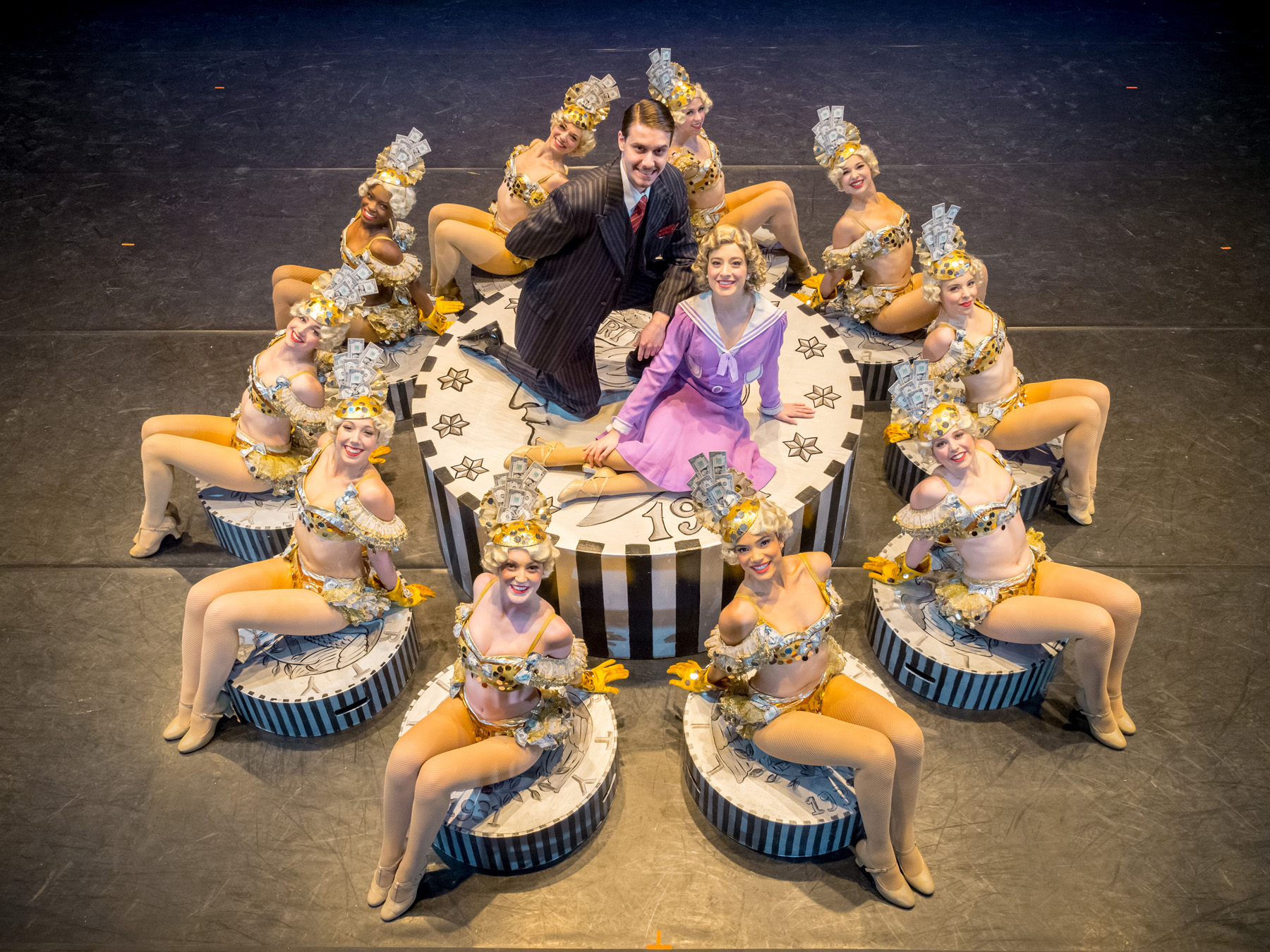 dancers surrounding a plinth on which two character actors are sitting