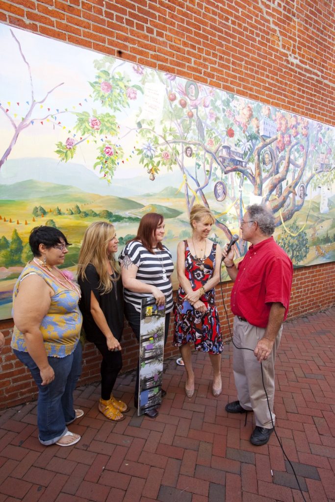 women being interviewed in front of mural