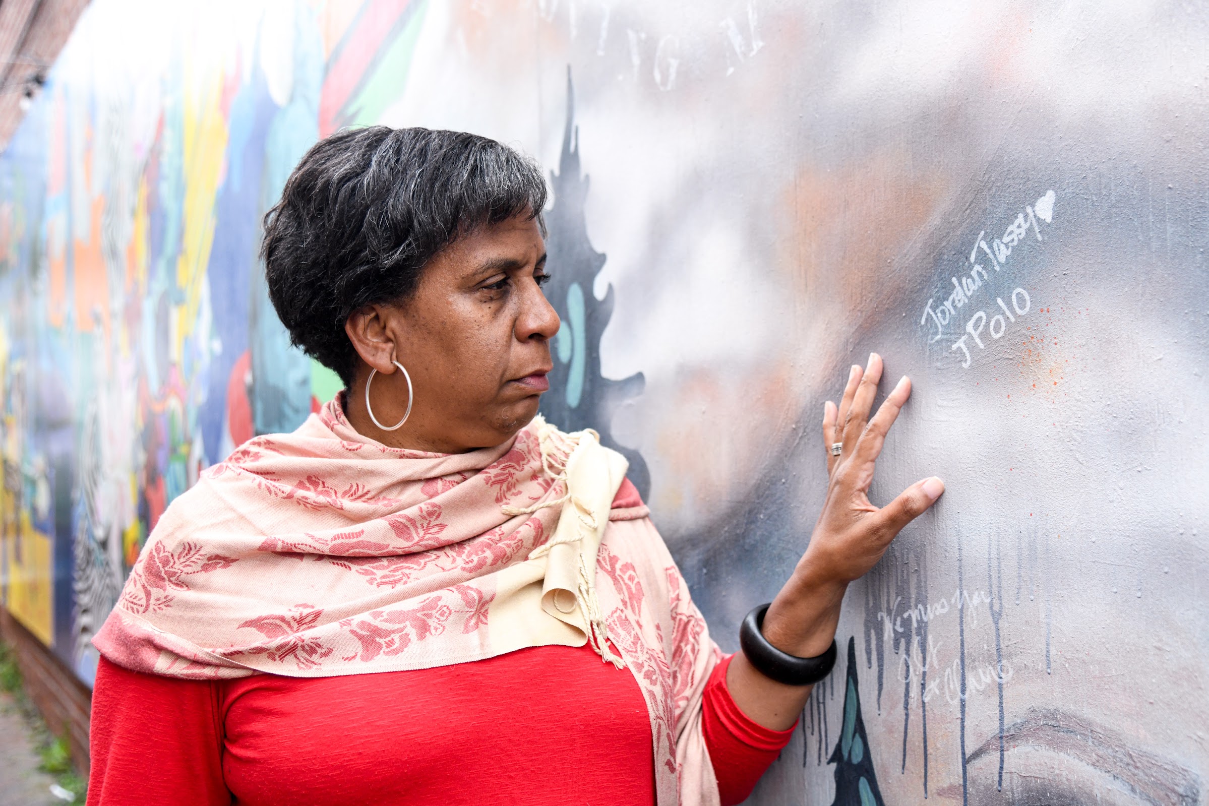 Normal Tassy stands by her son's name at the mural