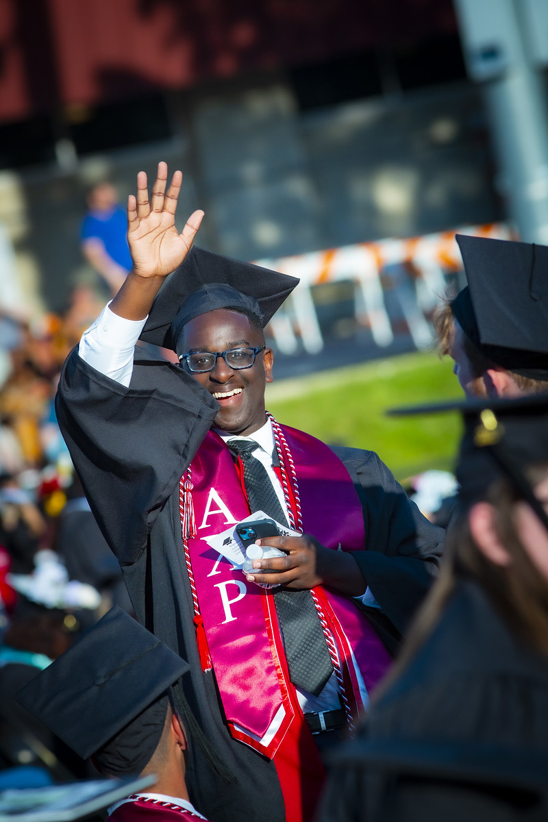 young bespectacled man in cap and gown waving