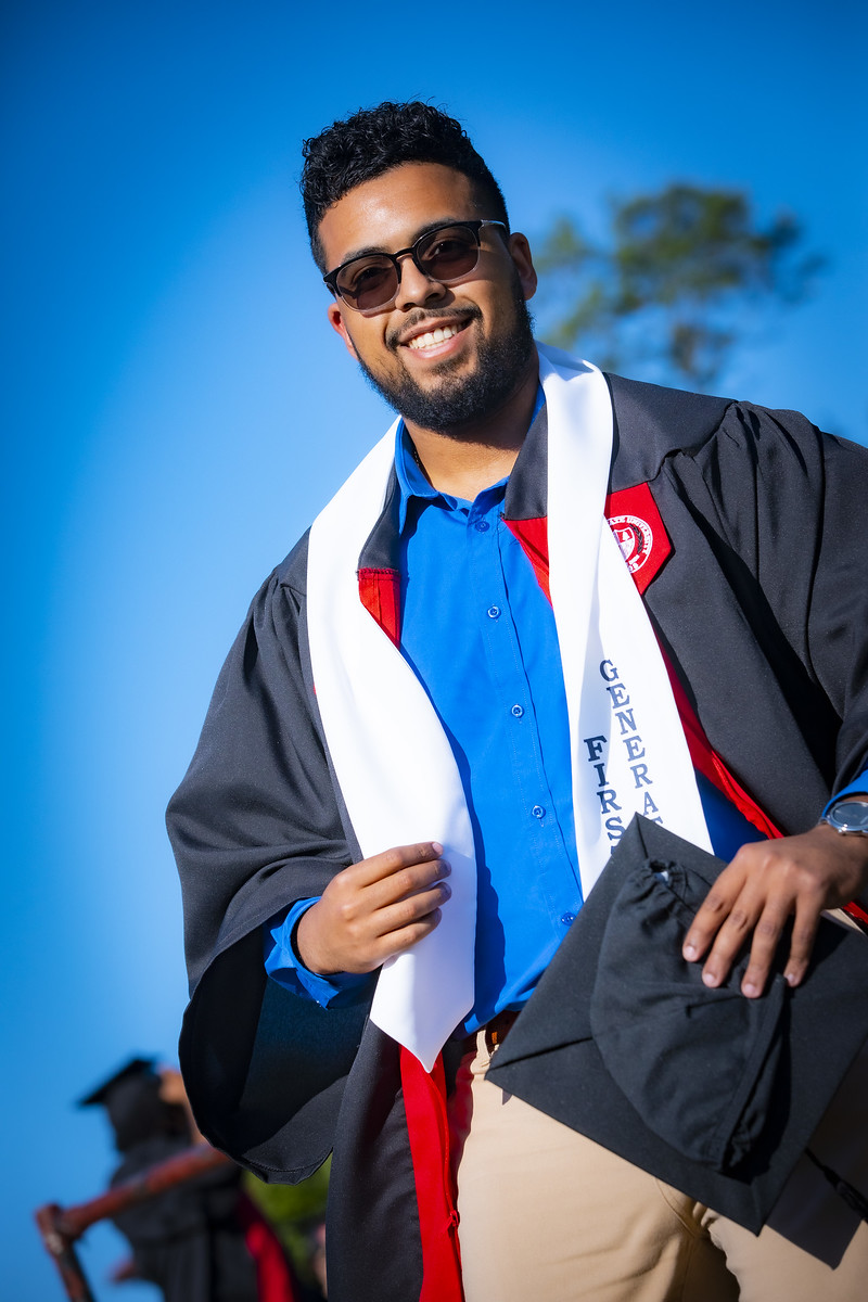 young man in sunglasses putting on graduation gown