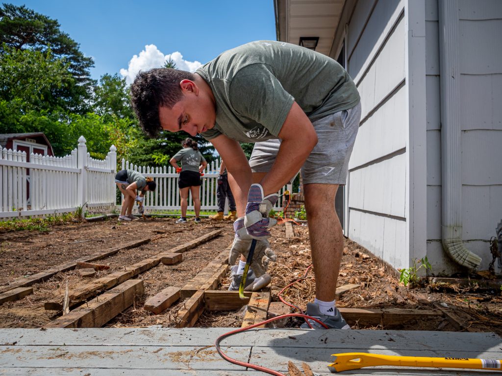 Young man using a crow bar to deconstruct an old deck