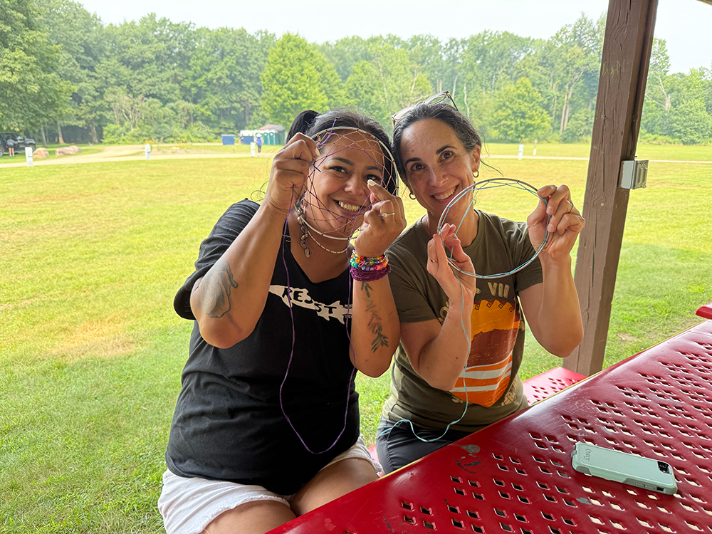 two women sit together outside showing dreamcatchers that they are making