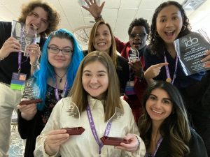 Seven people holding awards and smiling, standing in a half circle. 
