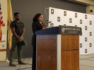 Female student speaks during the ceremony, with male student behind her.