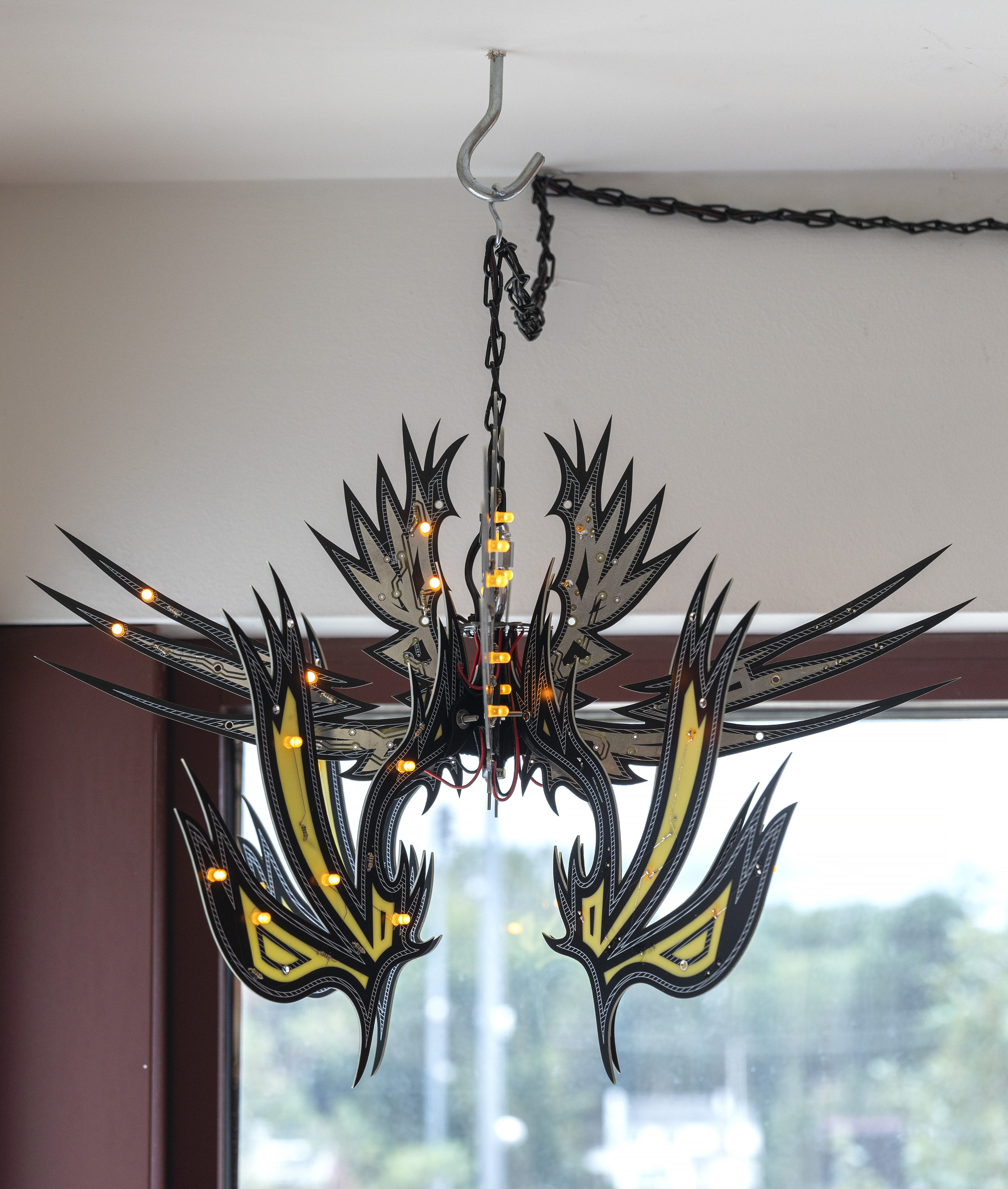 Installation photo of a small, black and yellow artwork with orange-yellow lights hanging from the ceiling, meant to mimic a lamp.