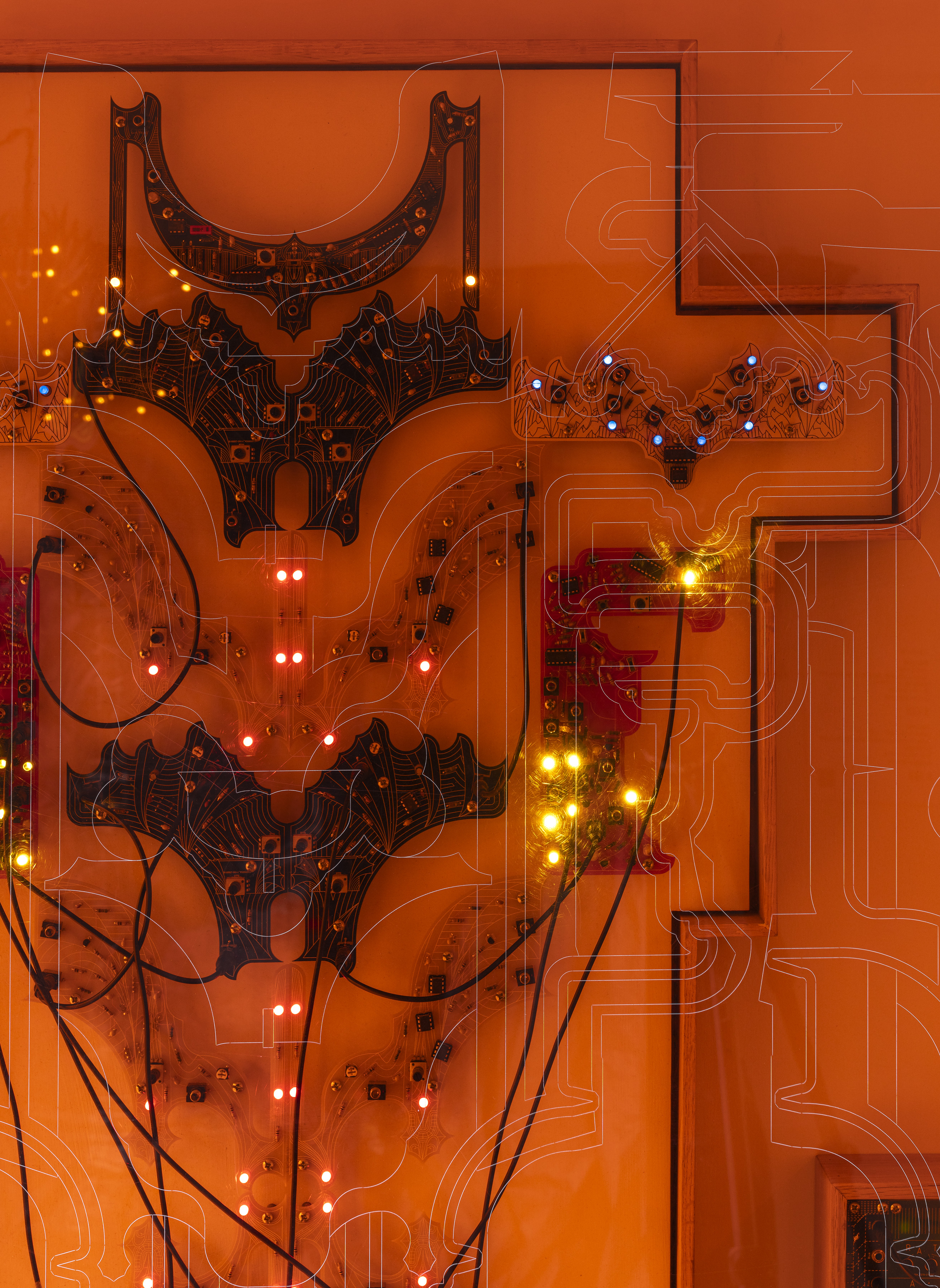 Close up shot of an artwork made of circuit boards and wires behind orange acrylic is affixed to the wall.