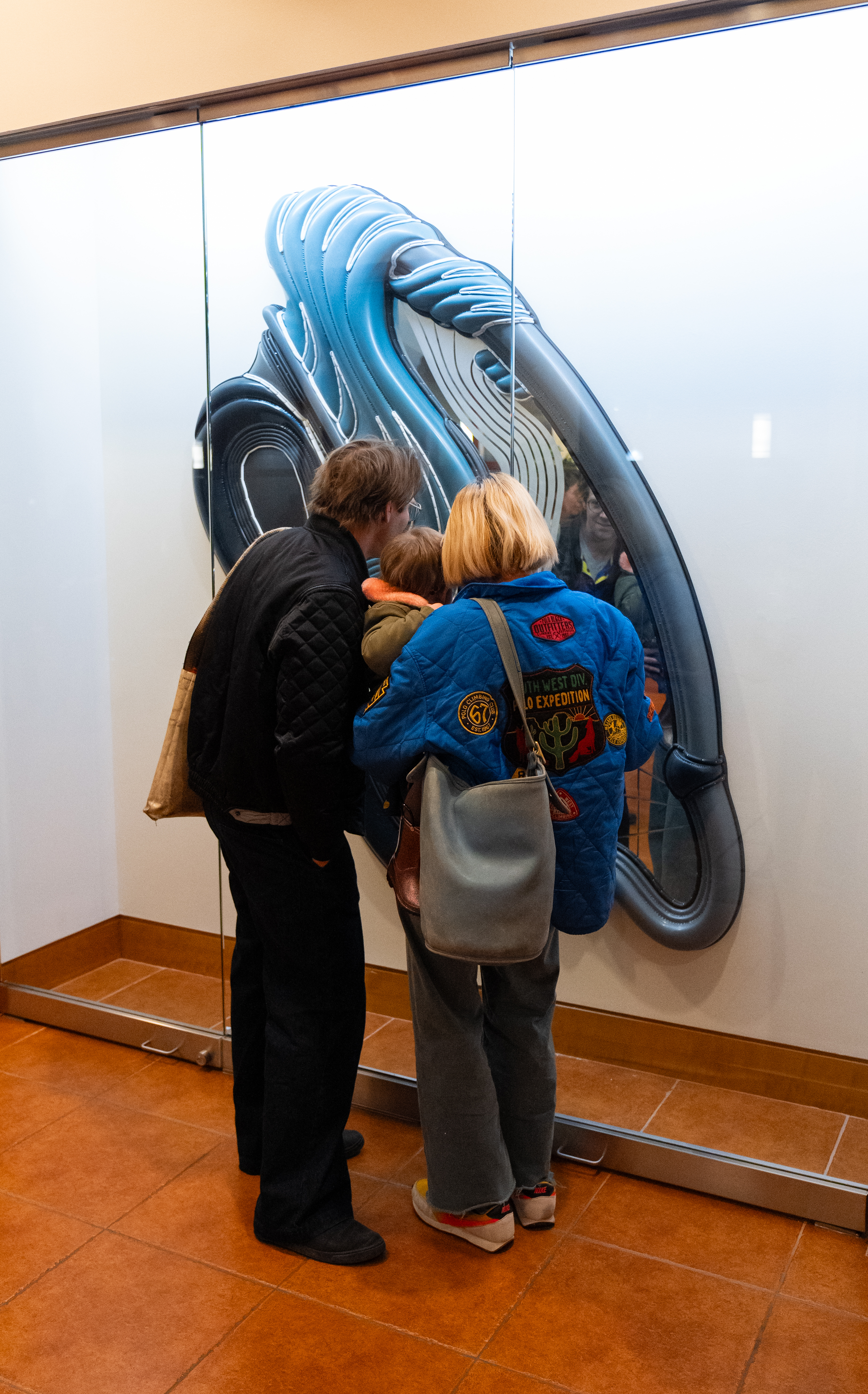 A family looks at a large blue artwork behind a glass case.