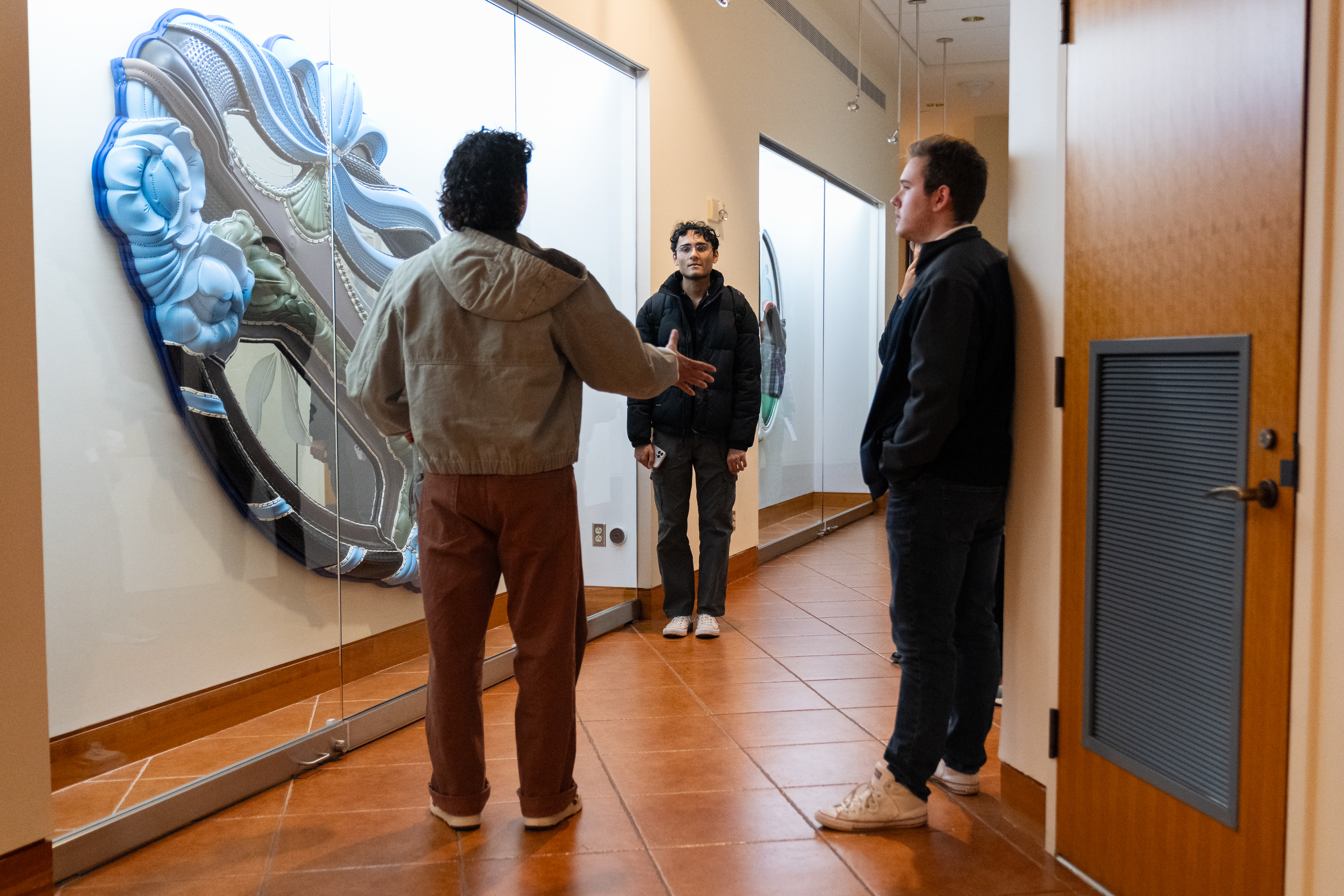 Three visitors converse next to a large blue artwork behind a glass case.
