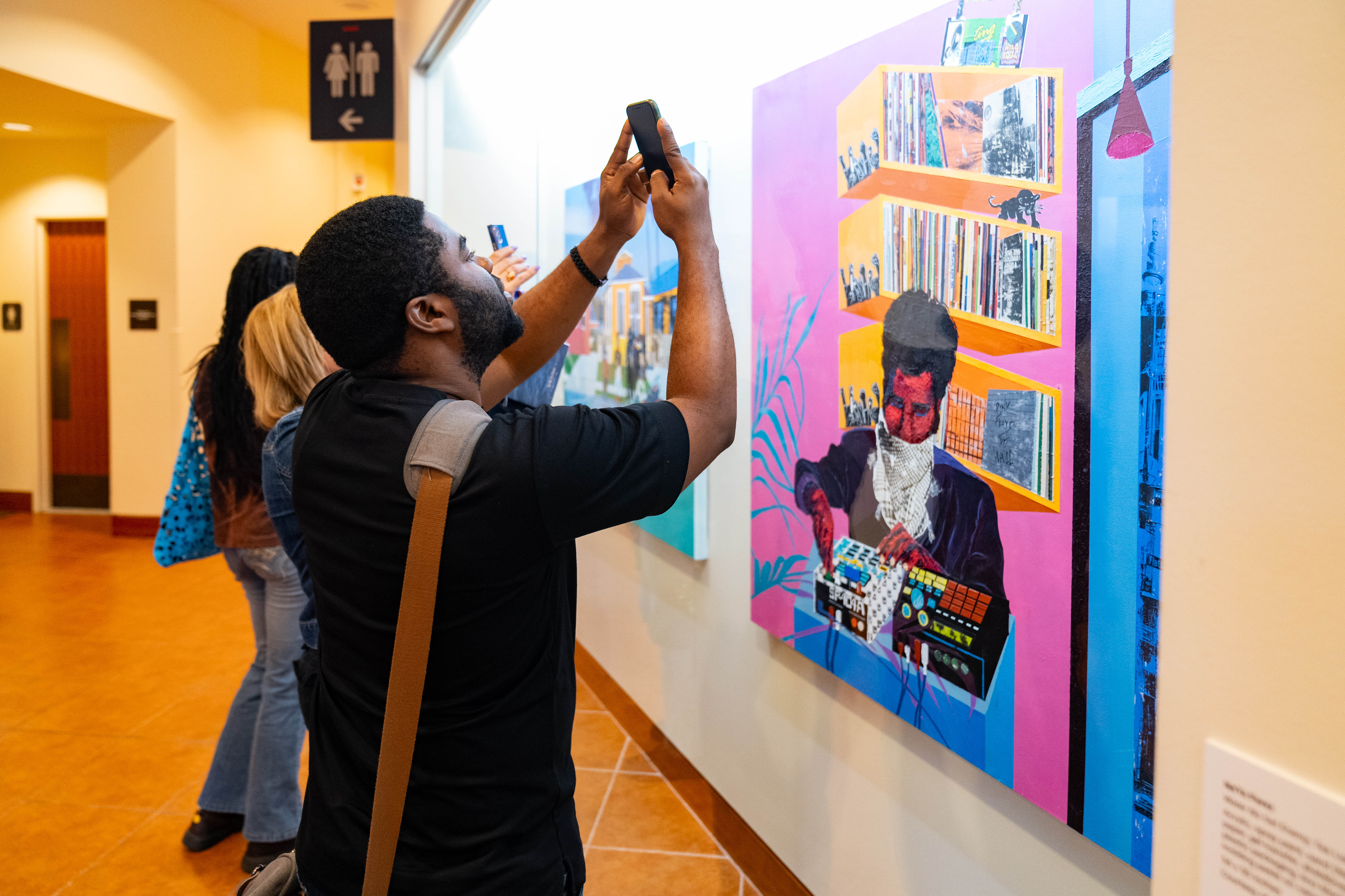 A visitor points their phone at a painting behind a display case.