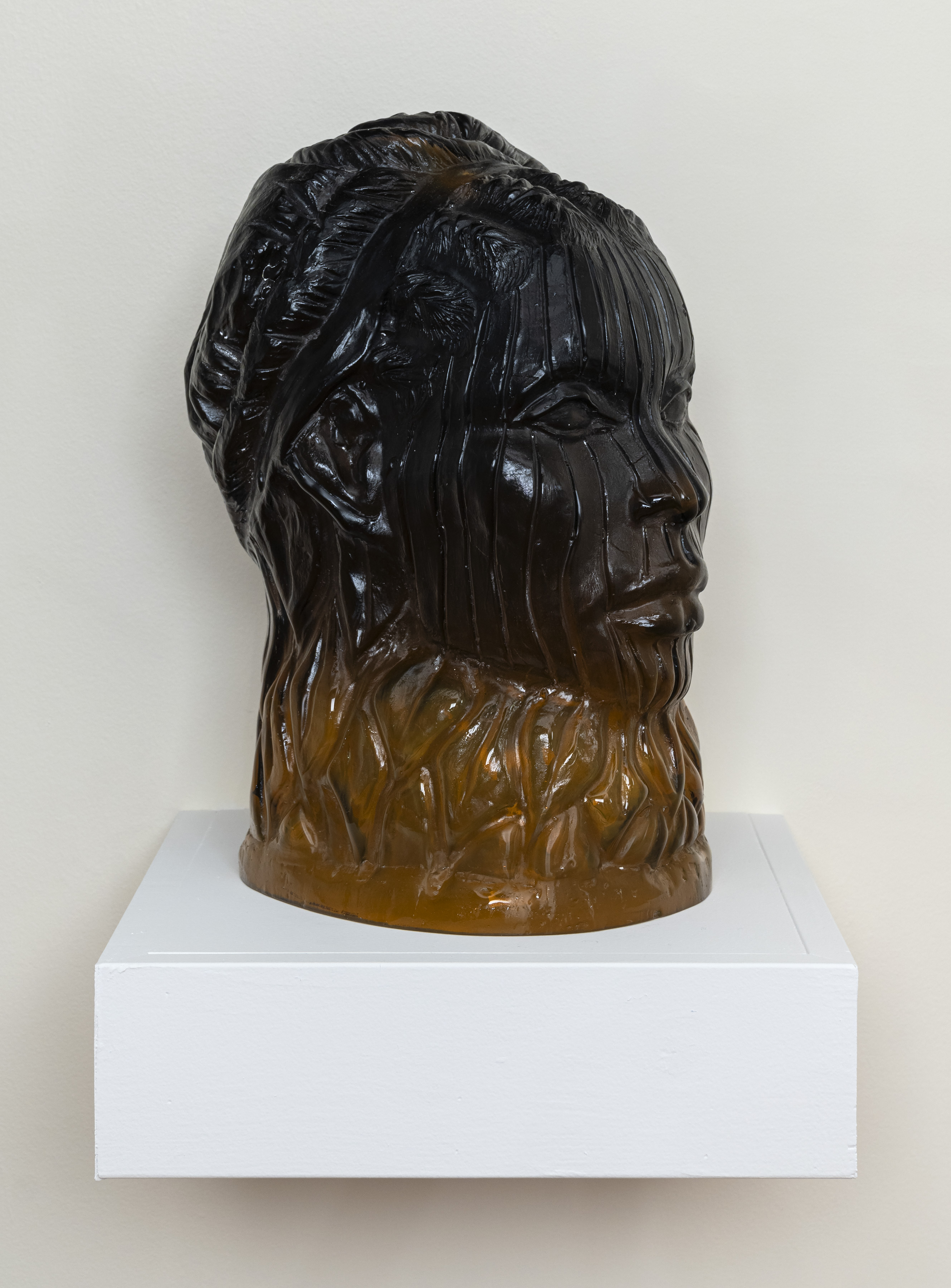 Close-up of a glass bust. The face consists of black glass and is wrapped in a gold-brown collar.