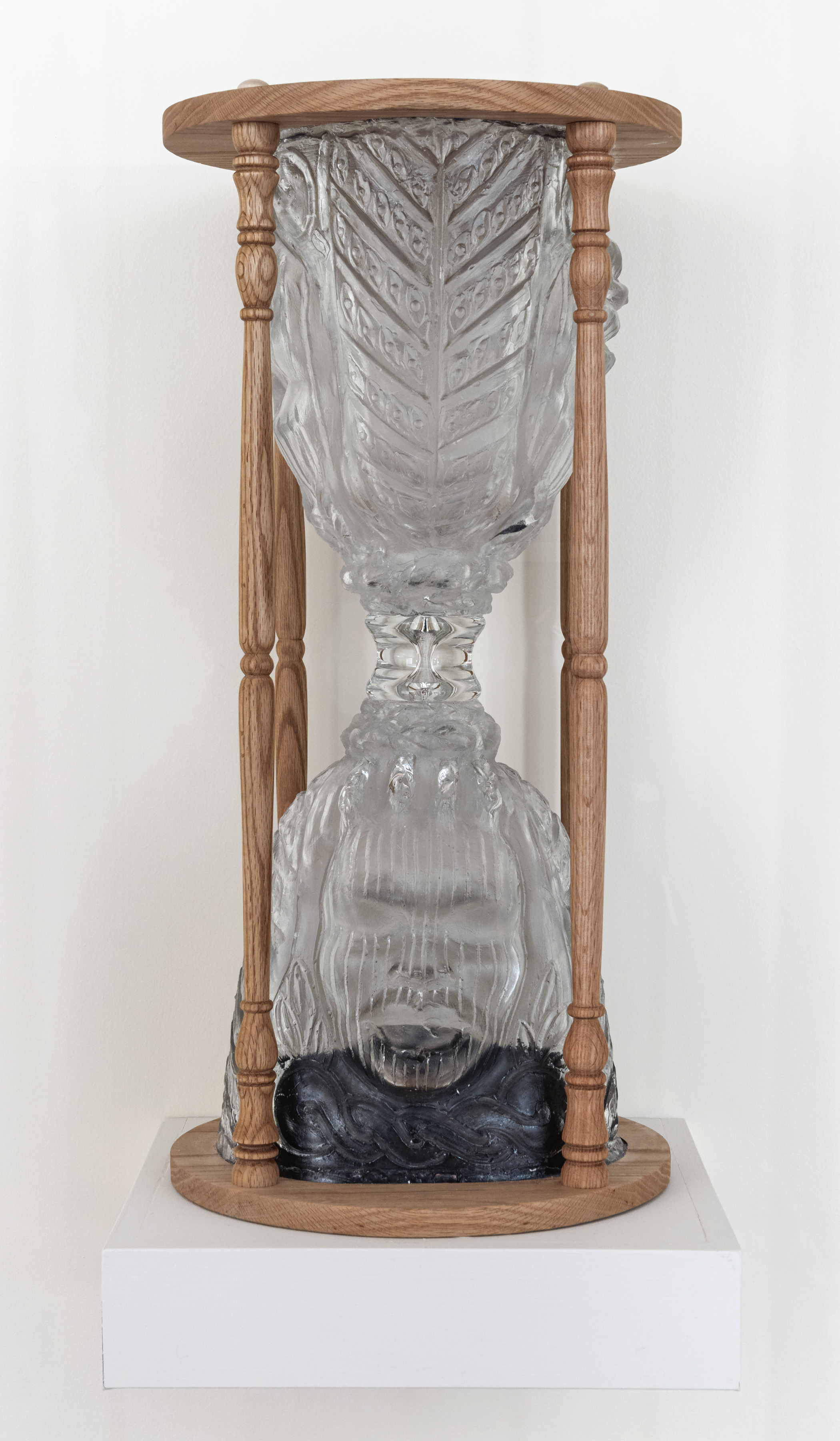 Close-up photo of a glass hourglass. Each half is made up of a face. Black sand sits at the bottom.