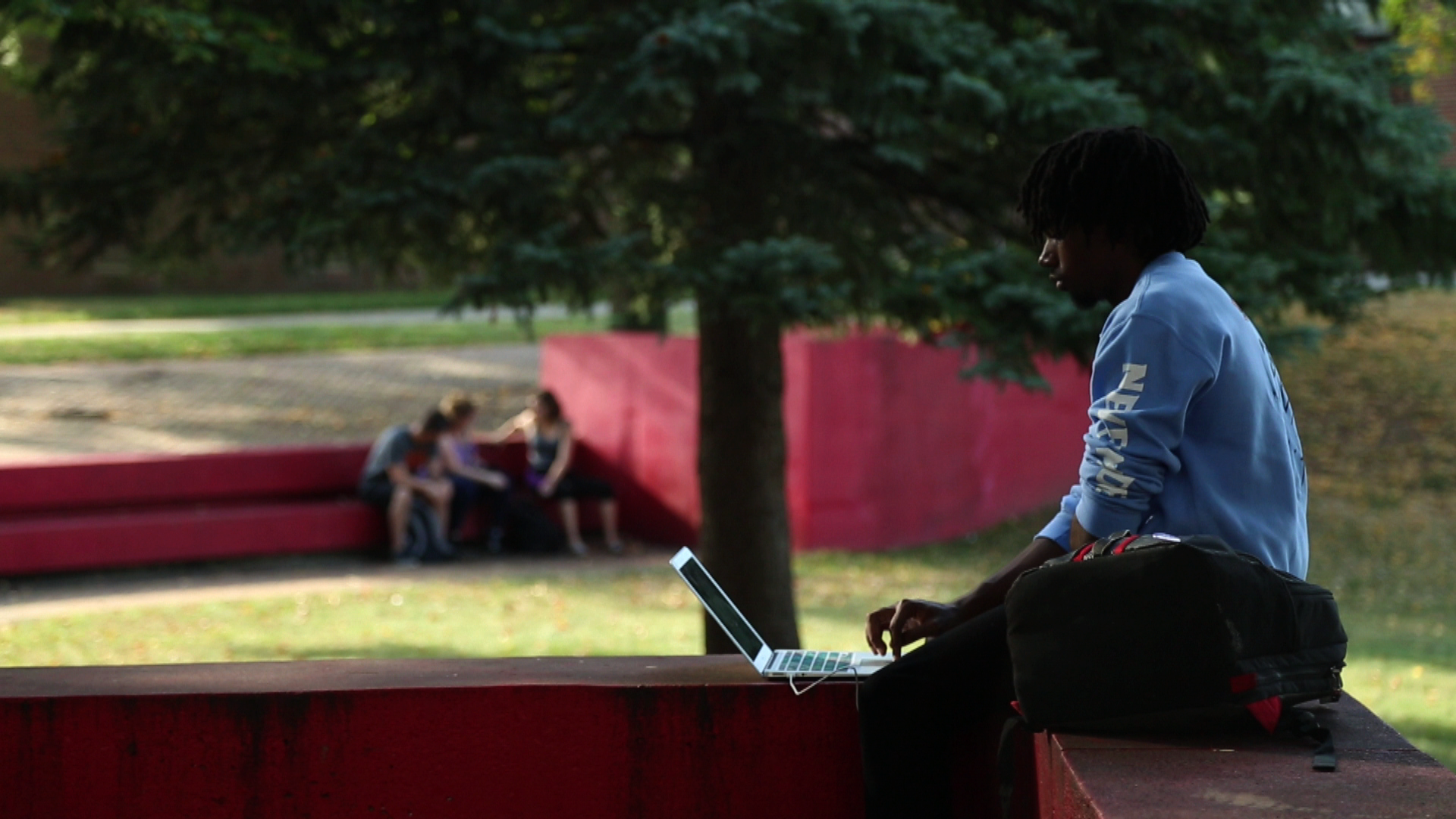 High school age male student sits outside on laptop doing work