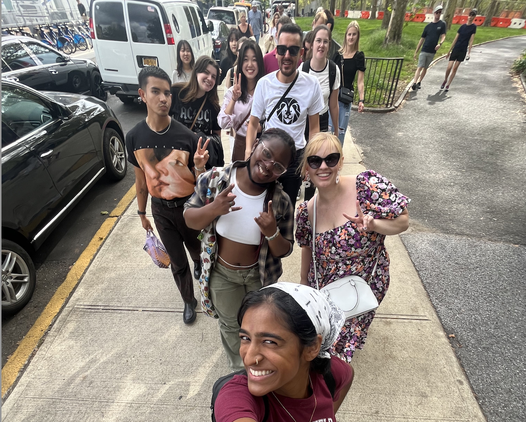 Group of student and their advisor from different cultures and countries smile together in a selfie in the streets of Brooklyn, NY