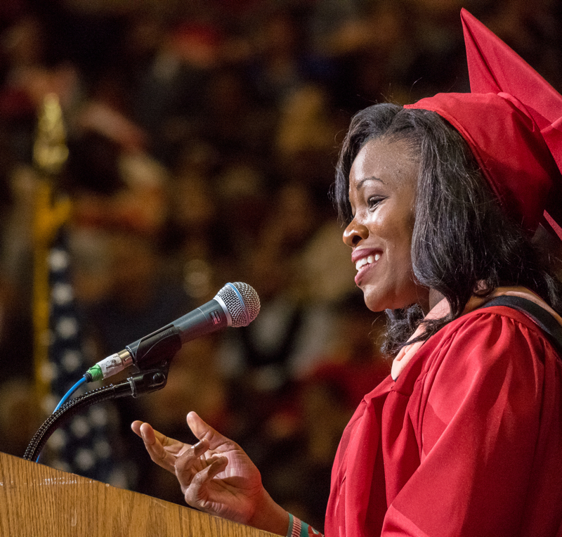 A woman clad in Montclair State University's graduation cap and gown making speech at podium.