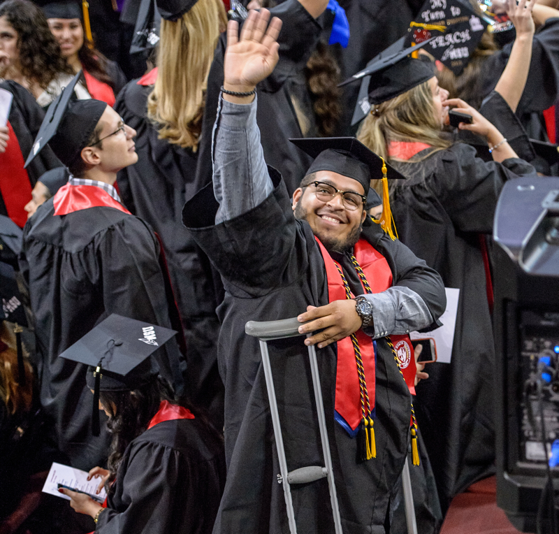 Montclair State University student on crutches waves at someone in the crowd.