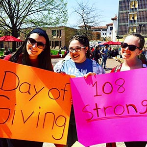 Three female Montclair State University students holding posters on Day of Giving.