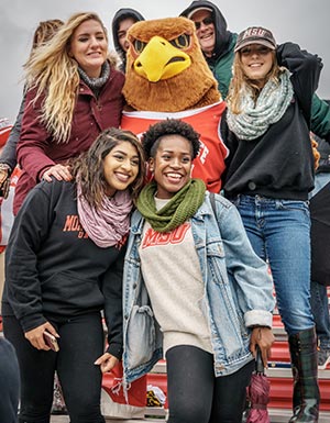 Female Montclair State University students posing with Rocky at Homecoming.