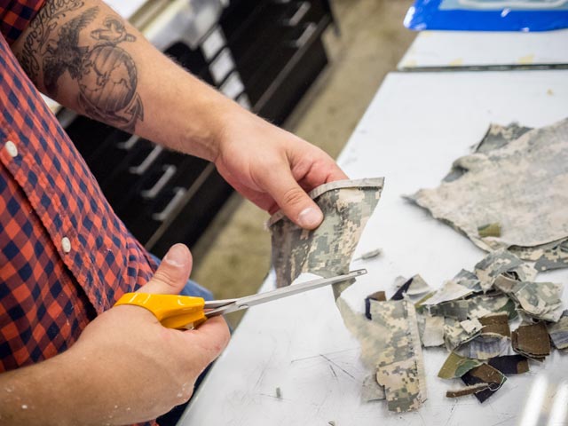 Photo of a veteran student cutting uniform cloth, preparing it to be made into paper.