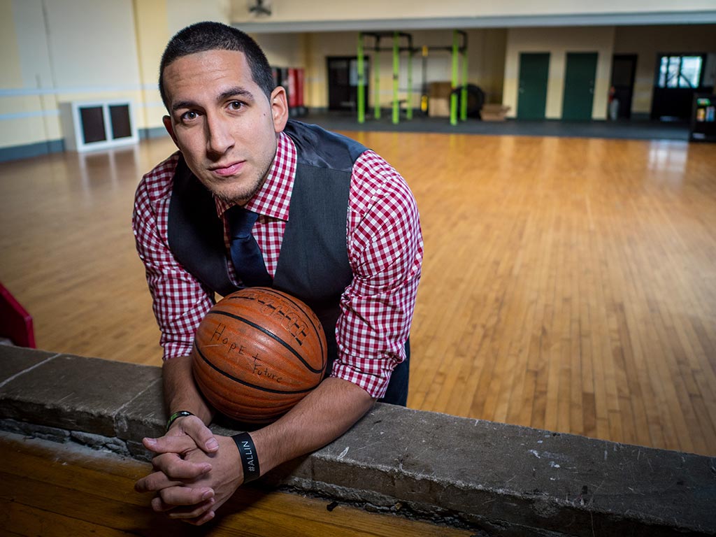 Gonzalez, wearing a checkered shirt with a tie and vest, holding a basketball in a gym.