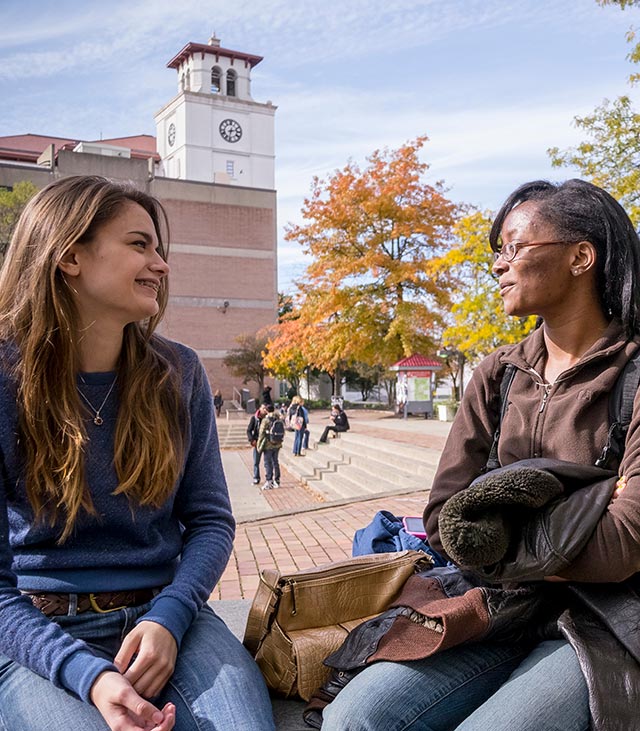 Photo of a pair of female Montclair State University students sitting down and chatting.