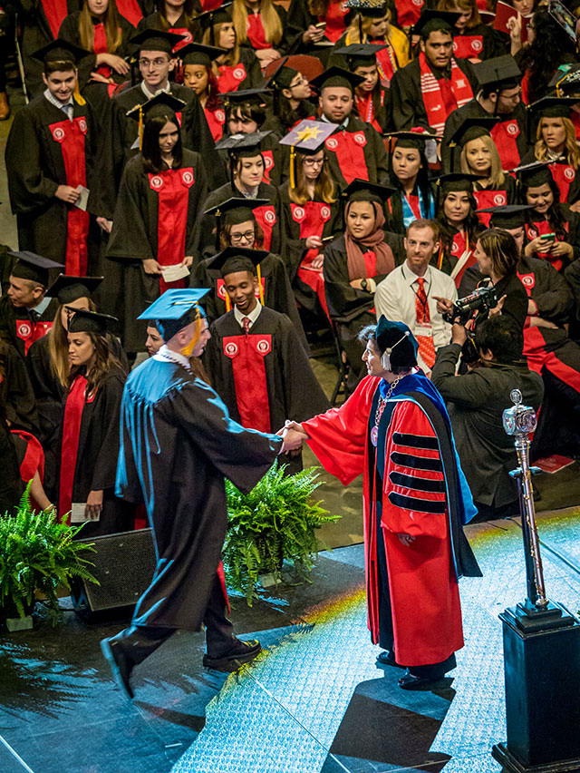 President Susan A. Cole greeting student as he crosses stage at Commencement.