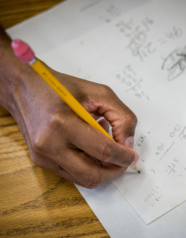 Hand writing math equations on paper with pencil.
