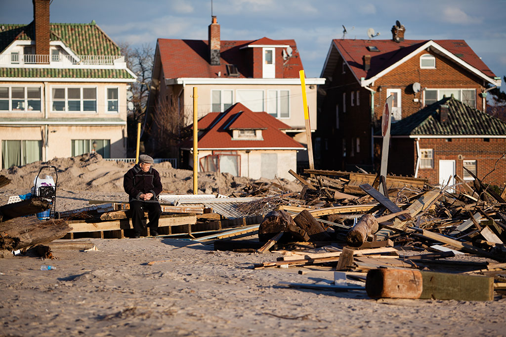 Elderly man sitting amidst ruins left by Hurricane Sandy.