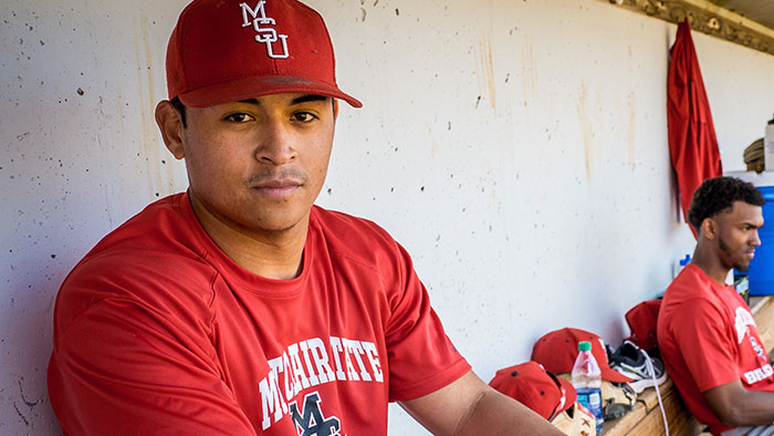 Photo of Jesse Baiza clad in baseball uniform sitting in dugout.