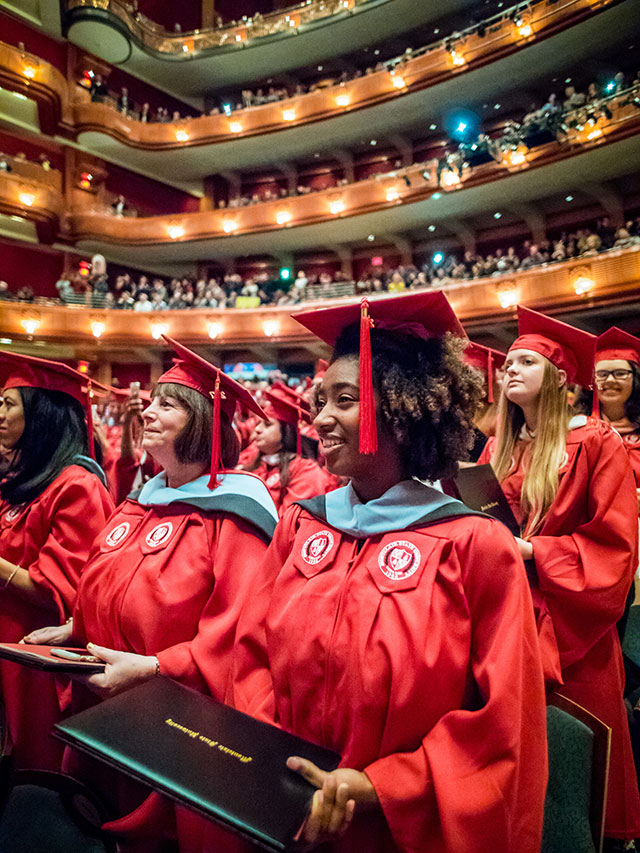 Female student clad in gown sitting in Commencement.