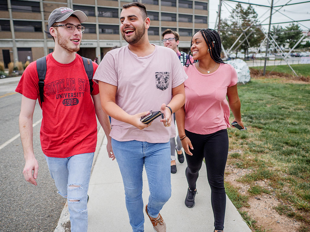 Three Montclair State University students walking and smiling.