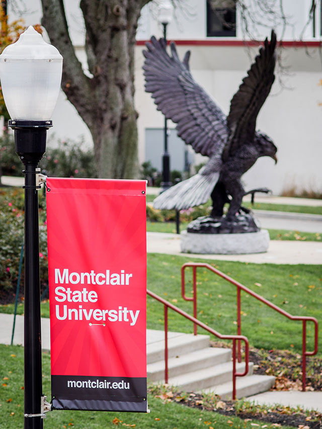 Montclair State University's banner on lightpole, with Red Hawk Statue in background.