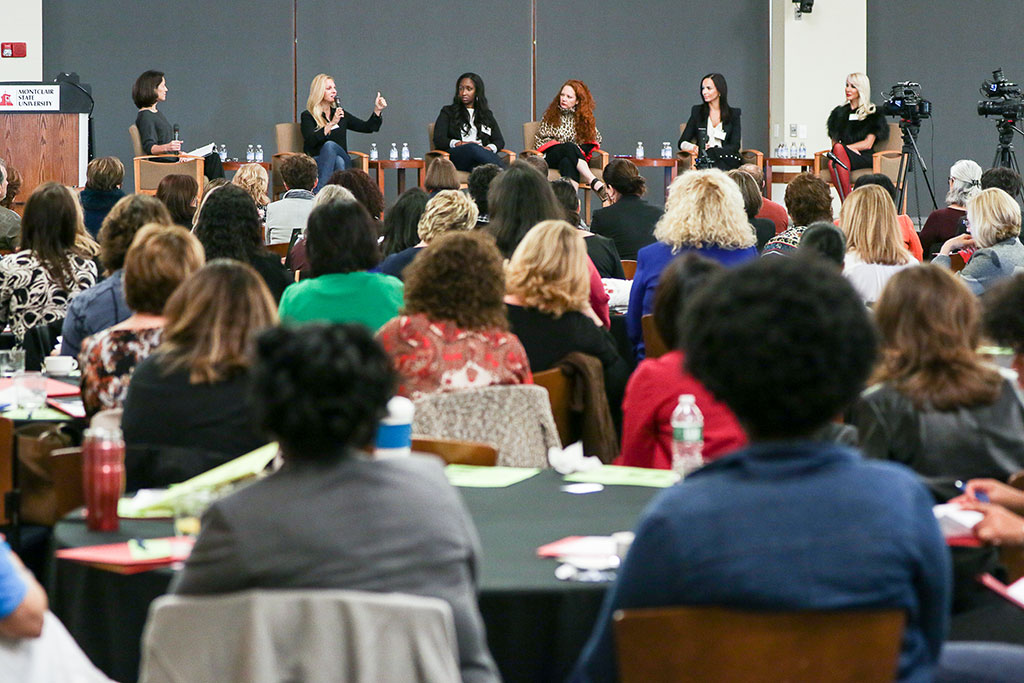 A panel of female entrepreneurs speaking in front of crowd.