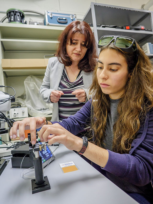 Rodica Martin, (left, with a student) studies optical properties that can be used in gravitational-wave detectors, which detect neutron stars colliding