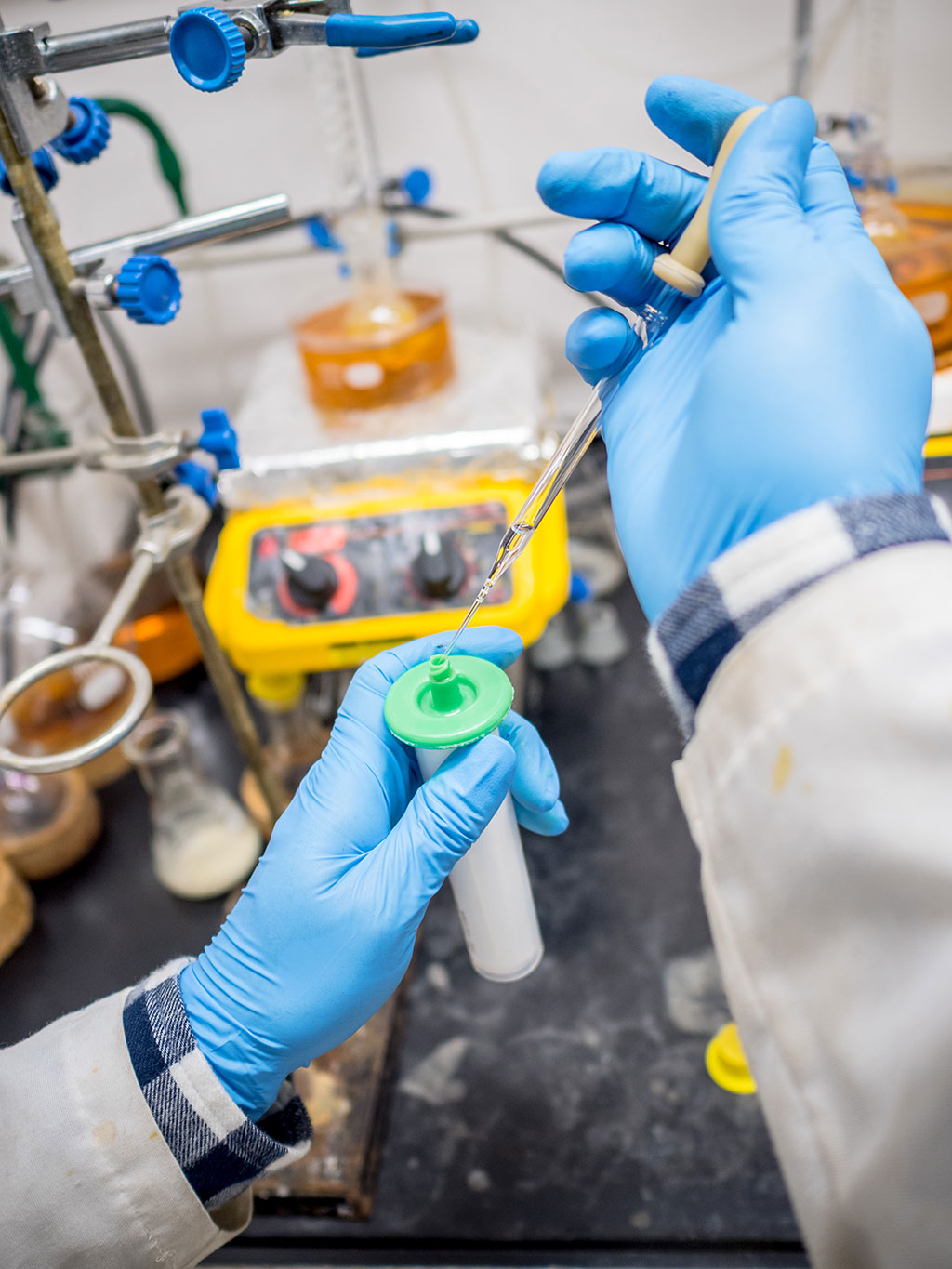 Gloved lab technicians hands injecting something into bottle