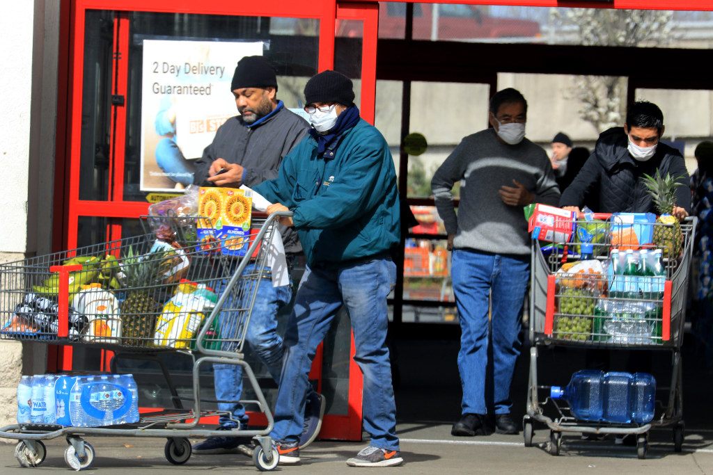 Shoppers stocked up on food supplies in Paramus. Many wore masks and gloves and practiced social distancing. Bottom: Hundreds of cars lined up at the Bergen Community College testing site predawn, before authorities closed down the entrances less than an hour before it reached “maximum capacity.”