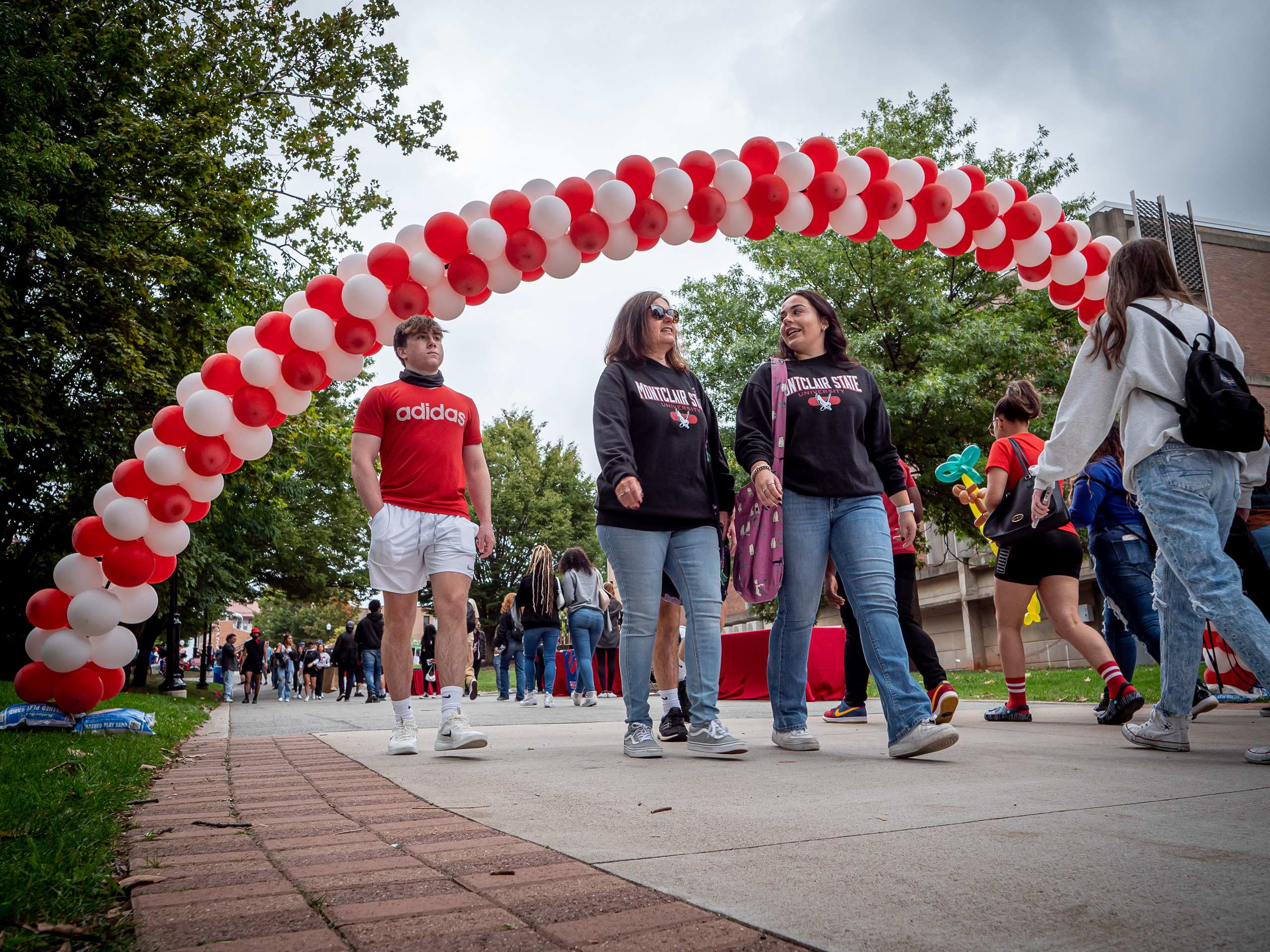 alumni and students walking below balloon arch on campus