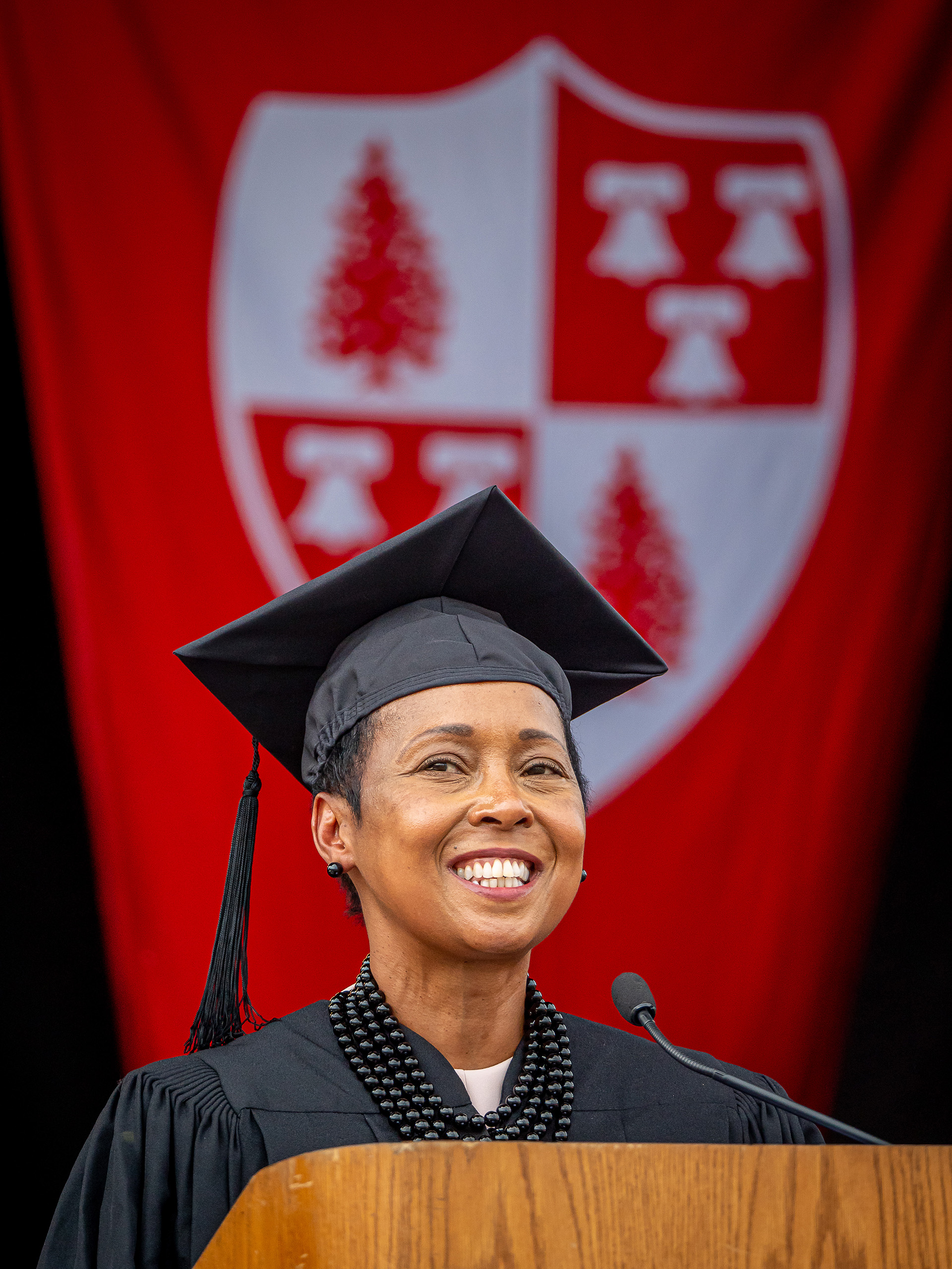 Wamwari Waichungo wearing cap and gown, speaking at podium