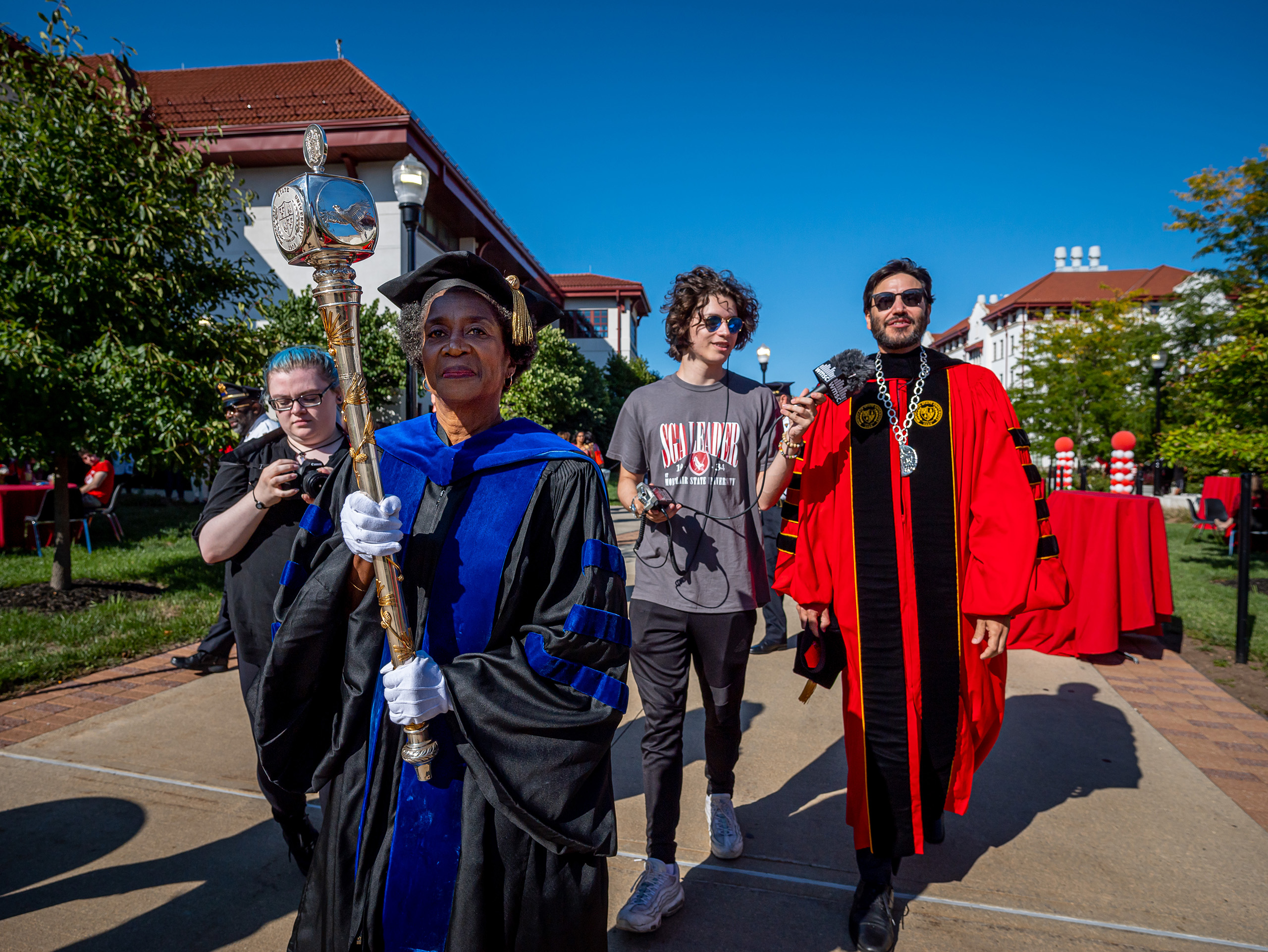 President Koppell walking toward the amphitheater in regalia being interviewed