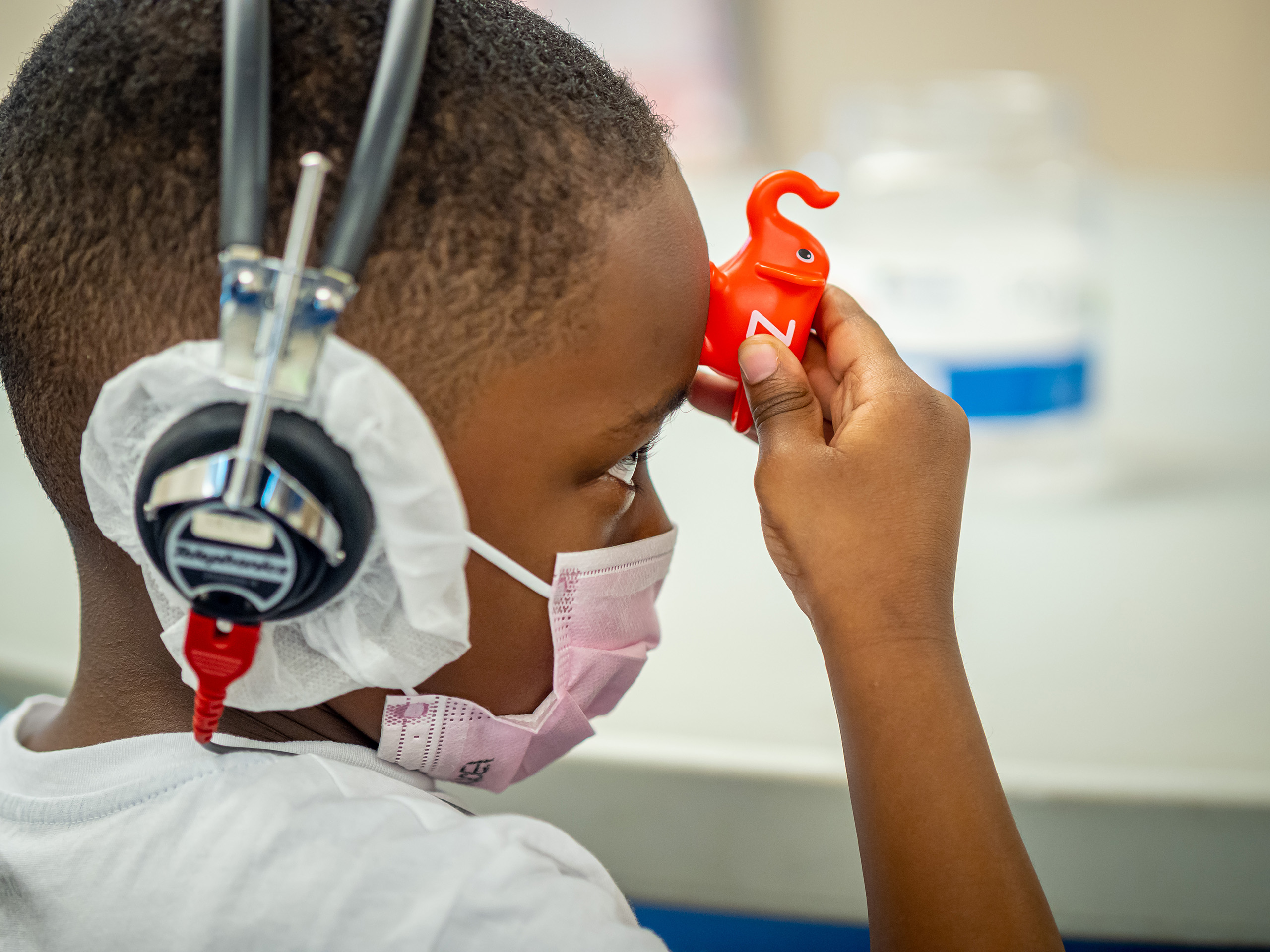 child wearing headphones holding a plastic elephant to his forehead