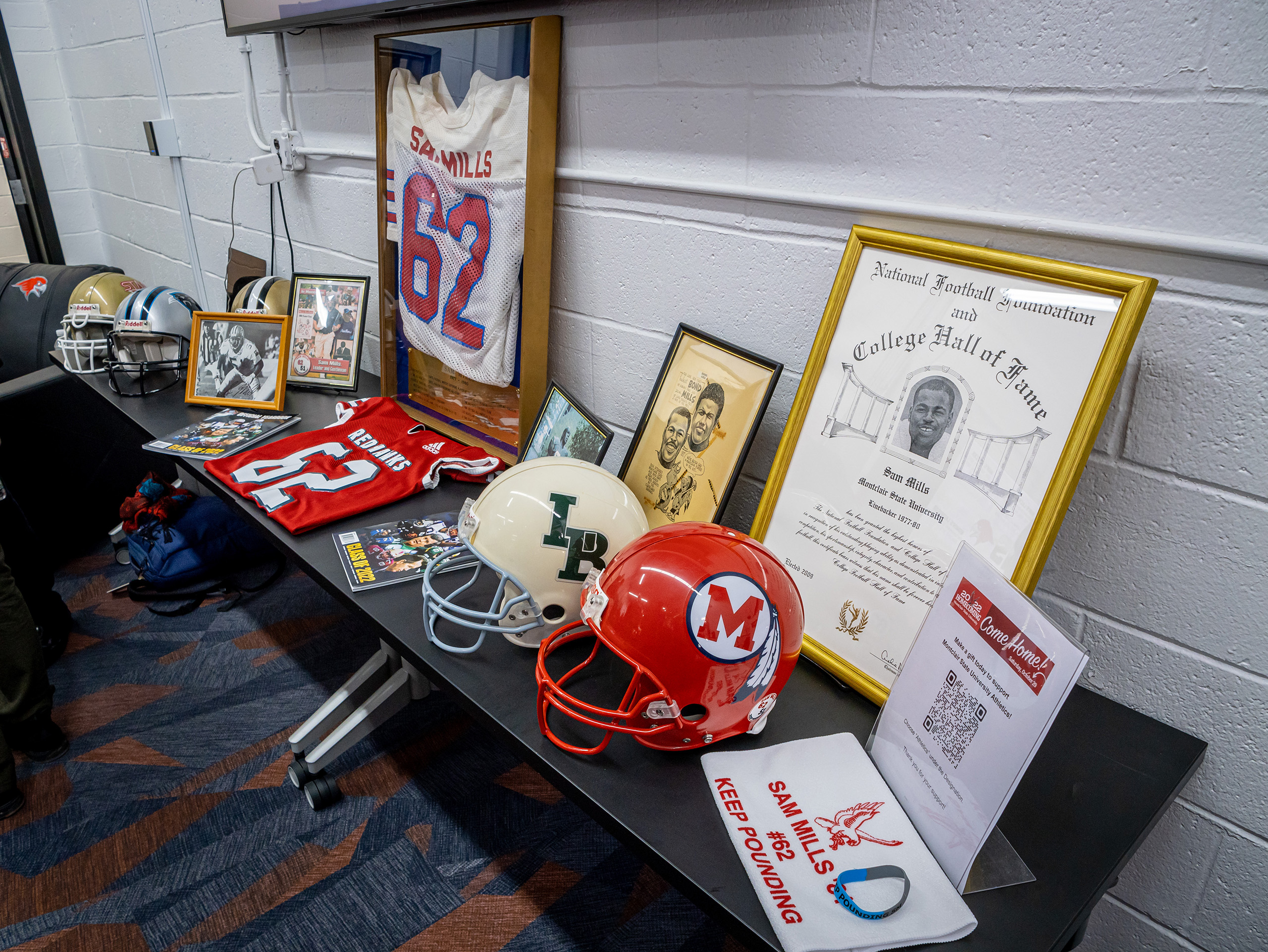 Sam Mills helmets, framed jersey, and other memorabilia on table