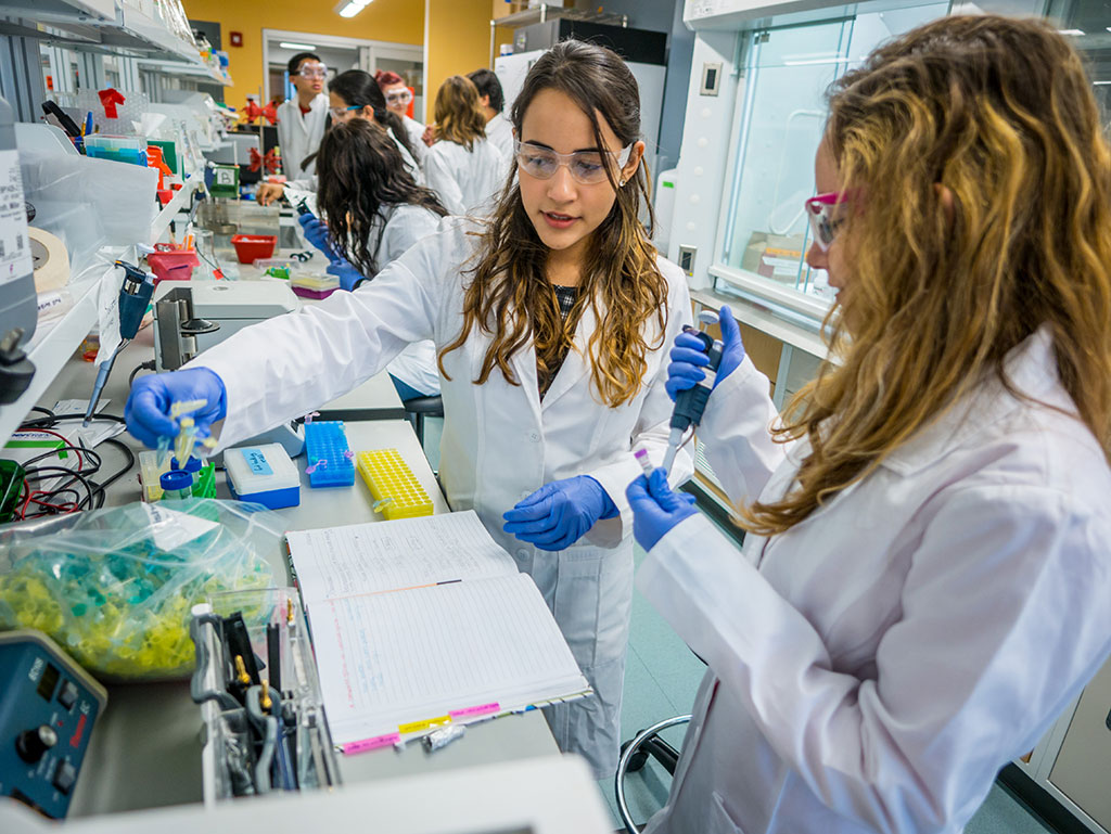 Two female Montclair State University students clad in lab coats doing experiments in a lab.