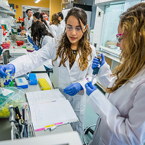 Two female Montclair State University students clad in lab coats doing experiments in a lab.