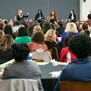 A panel of female entrepreneurs speaking in front of crowd.