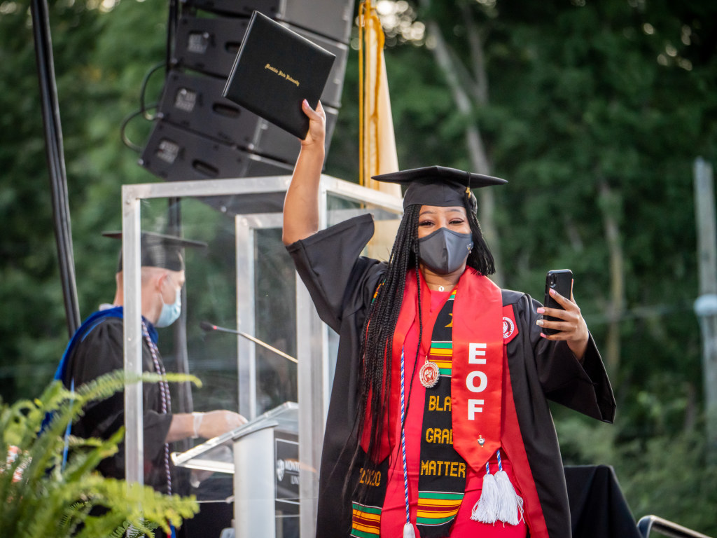 Student wearing cap and gown at Commencement raising diploma into the air