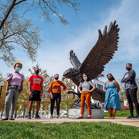 Six students in masks standing outside in front of Montclair State's hawk statue