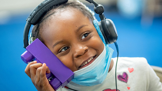 young child holding block while wearing headphones