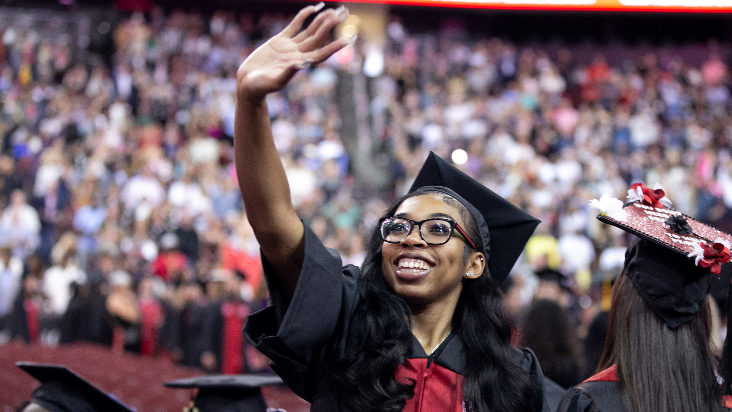 graduate wearing cap and gown waves (Photo by Aristide Economopoulos)