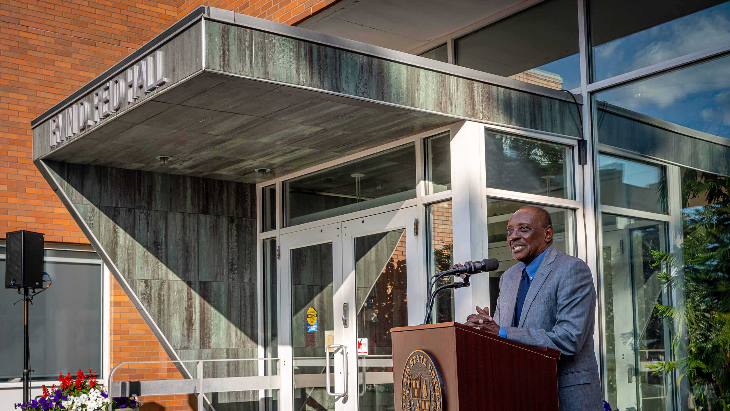 President Irvin D. Reid stands at a podium in front of the newly named Irvin D. Reid hall